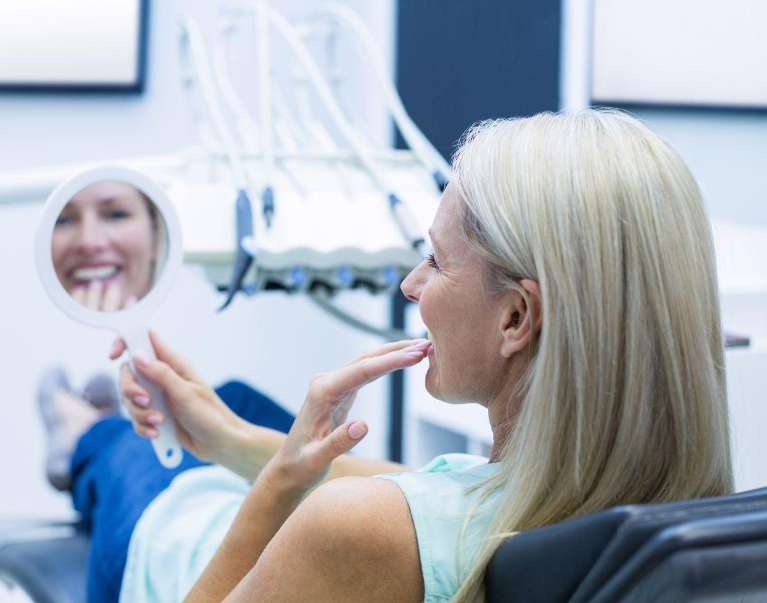 woman sitting in a dental chair while holding a mirror
